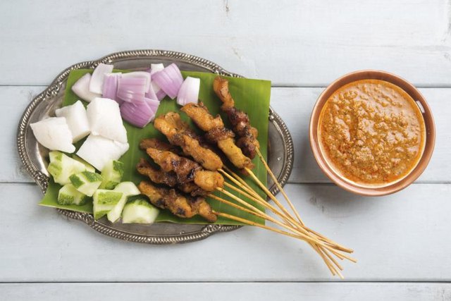 Chicken satay on skewers with a bowl of peanut sauce.