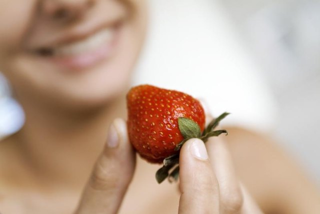 A woman holding a strawberry.
