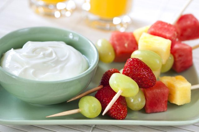 Skewers of fruit with a bowl of yogurt on the side.