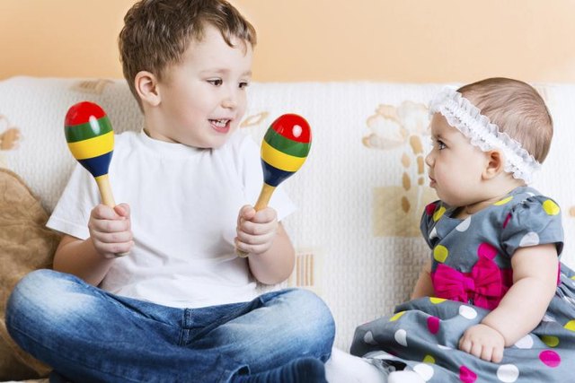 Toddler on sofa playing maraccas beside sibling.