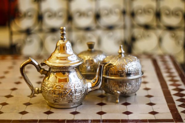 A metal Moroccan tea set on a tile table top.