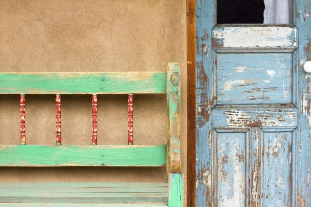 A weathered bench next to the front door of an adobe home.