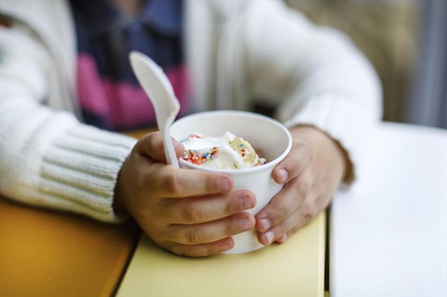 Hands of a toddler holding a cup of yogurt.