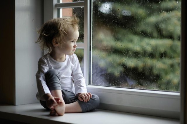 A toddler watching the rain fall from an indoor window.