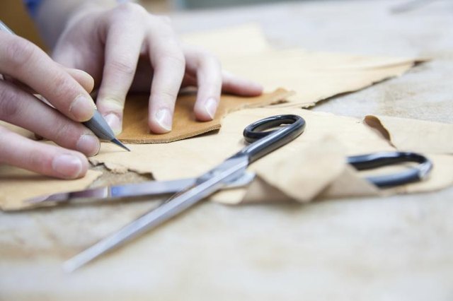 Close-up of a craftsman's hands measuring and cutting pieces of bonded leather.