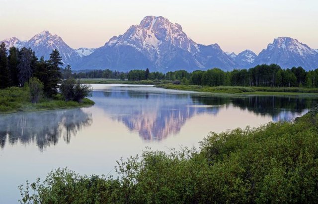 The Tetons are reflected on a stream in Wyoming.