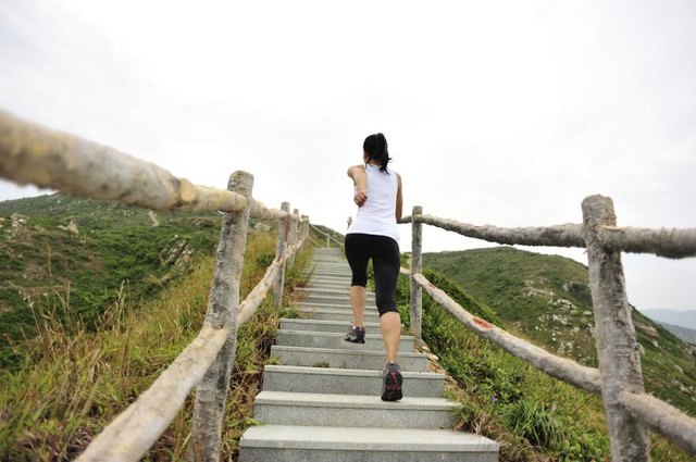 A woman jogging up a flight of stairs in a natural outdoor setting. A woman jogging up a flight of stairs in a natural outdoor setting.