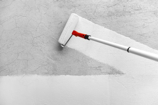 Roller spreading white paint on a gray wall