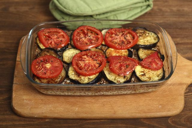 A glass baking dish is being used to roast tomatoes and eggplant
