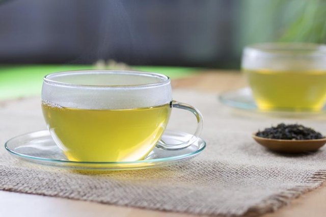 Two glass cups of plain hot green tea with a small bowl of dried tea leaves.