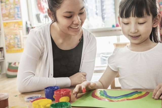 A young woman is helping a little girl with arts and crafts.