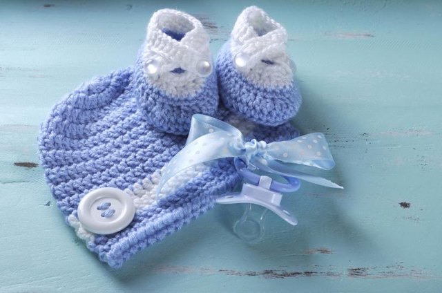 Hand-knitted baby blue hat and booties on a table with a pacifier. Hand-knitted baby blue hat and booties on a table with a pacifier.
