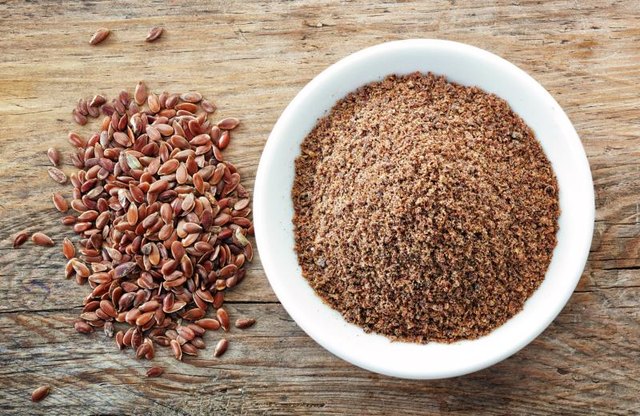 A bowl of crushed flaxseeds next to whole flaxseeds
