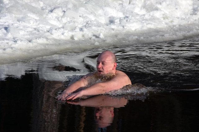 A man swimming in water next to ice and snow.
