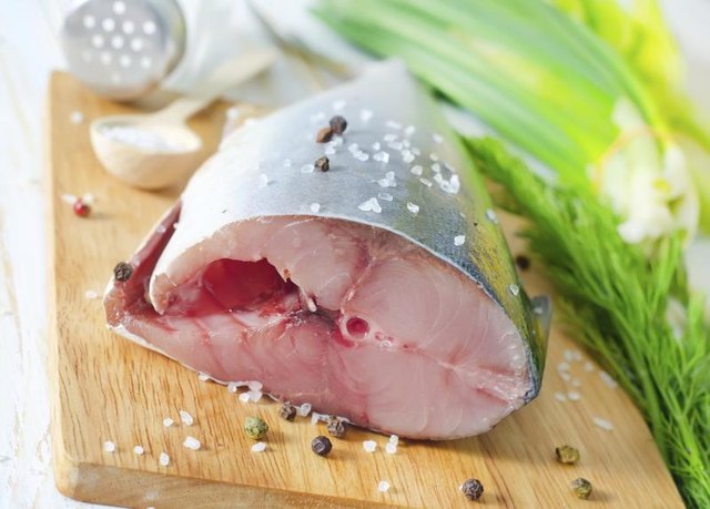 A slab of raw fish on a cutting board with salt, pepper and fresh dill.