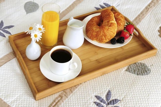 A tray with coffee and breakfast on the edge of a bed.