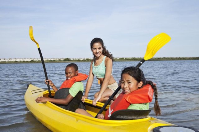 A summer camp counselor is helping young girls learn how to kayak.
