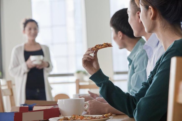 A woman joining a group eating pizza at a table.