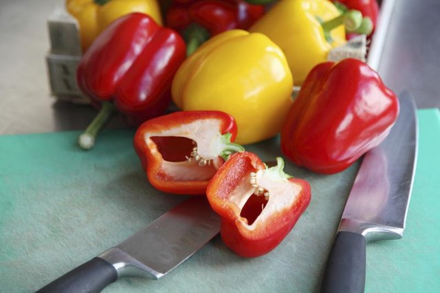Red and yellow bell peppers on a cutting board with chopping knives.