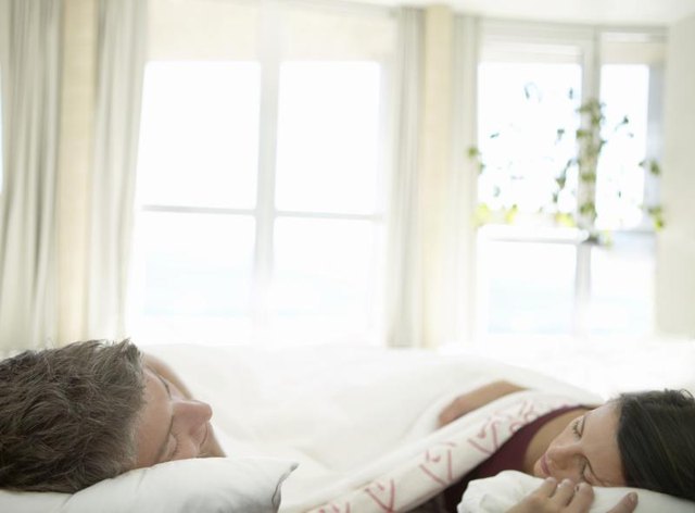 A couple sleeping with morning light shining in the windows.