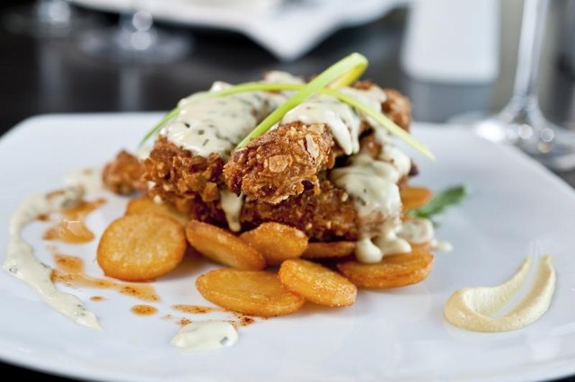 A gourmet plate of fried chicken strips and fried potato rounds topped with a creamy herb dressing.