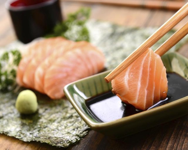 A close-up of a person dipping fresh salmon sashimi in soy sauce.