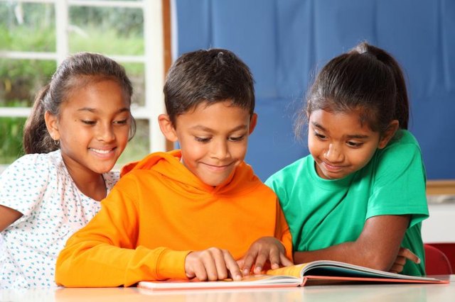 A small group of three children sit and read together