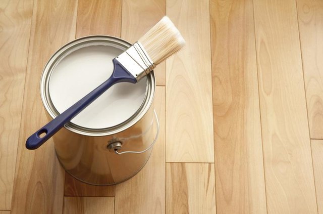 Can of white paint with brush on a wood floor.