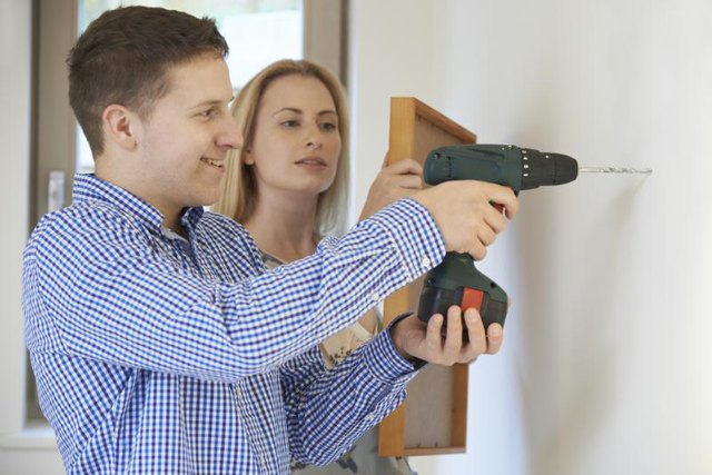 A couple is drilling into the wall to hang a photo.
