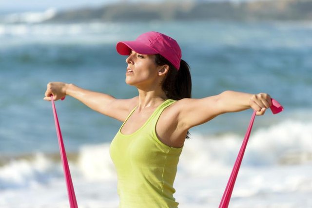 Young woman using a resistance band on the beach.