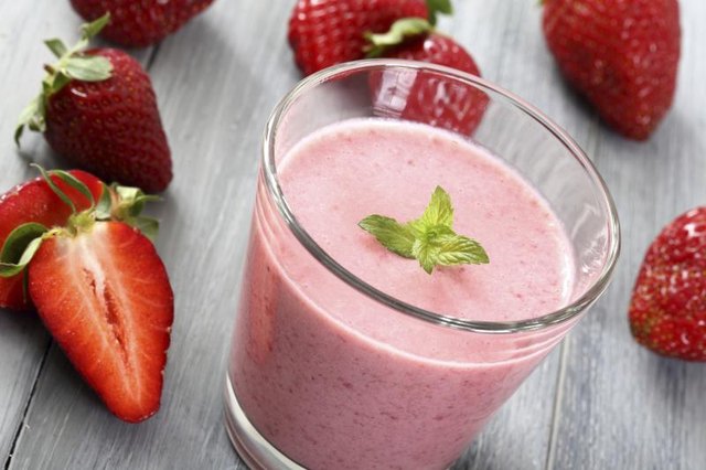 Strawberry smoothie in small glass, surrounded by whole strawberries.