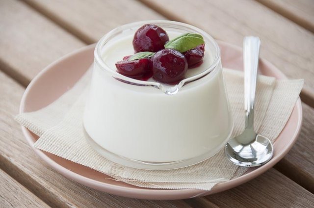 Fresh yogurt topped with cherries on a table.