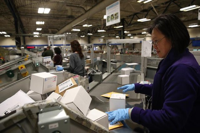 A postal worker sorts through packages at a distribution center