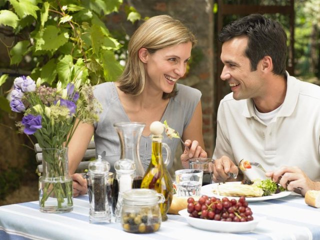 Couple eating lunch at outdoor table with salad on their plates.