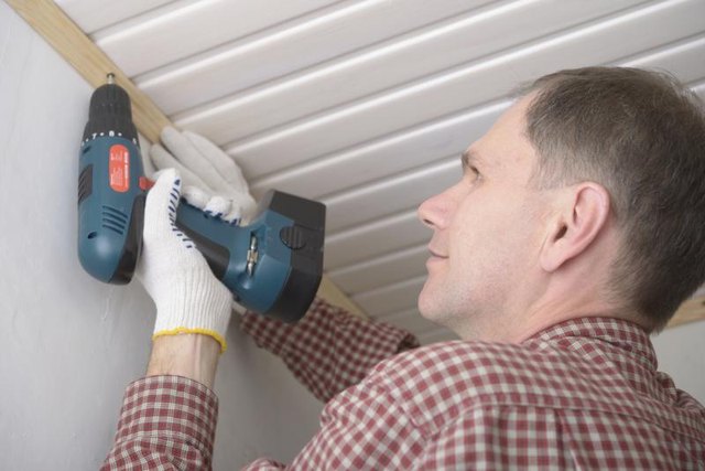 A man is attaching molding to his ceiling using an electric screwdriver.