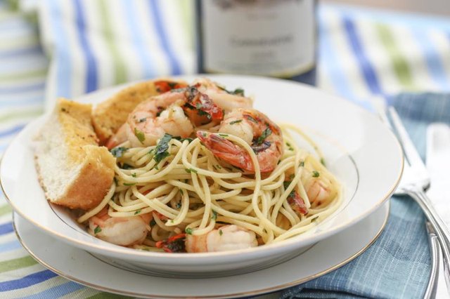 A pasta dish topped with shrimp and garlic bread.
