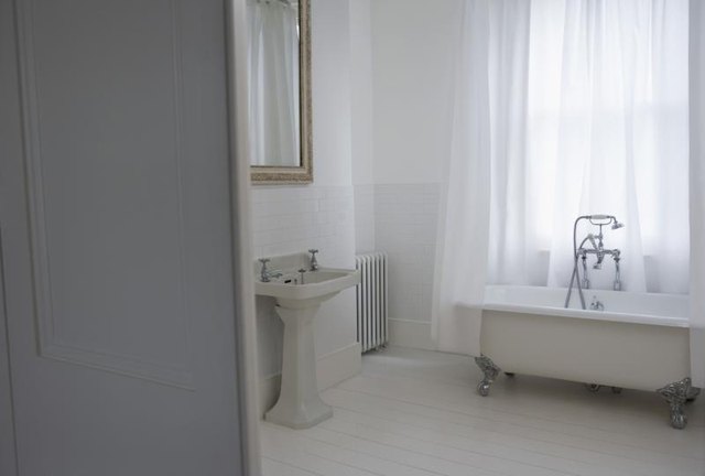 A sheer white shower curtain around a clawfoot bathtub.