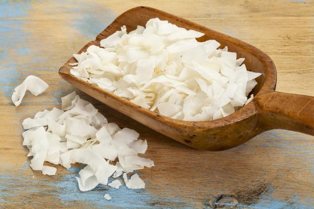 Shredded coconut flakes in a wooden spoon, laying on a rustic table.