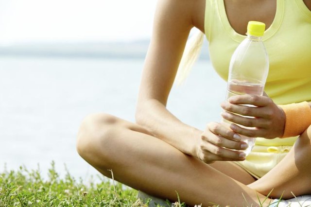 A close-up of a runner drinking water in a park by the lake.