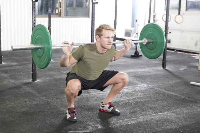 A man performs a squat at a gym.