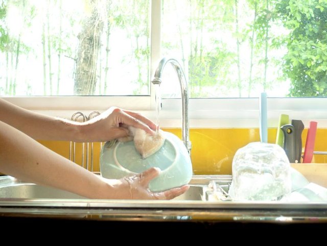 A young woman washes the dishes with a sponge and soap and water