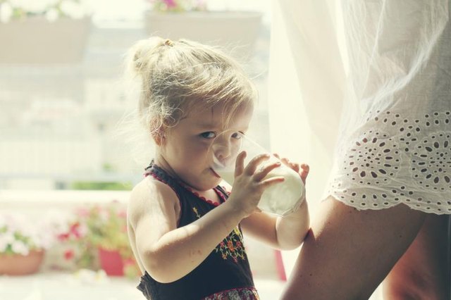 Toddler by her mom's leg drinking milk