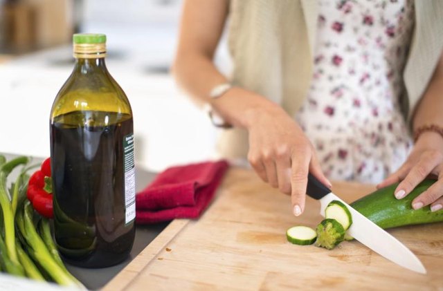 A young woman uses a chopping knife to cut a cucumber