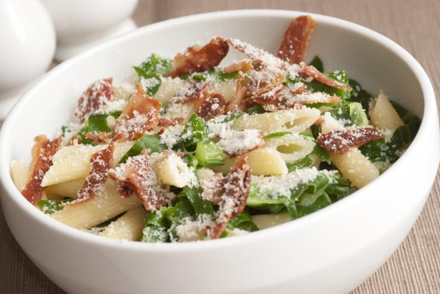 Penne pasta with shredded kale, bacon pieces and cheese