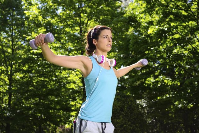 A woman outside performing shoulder exercises.