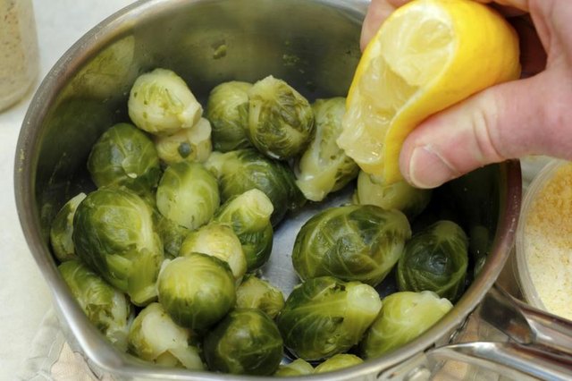 Hand squeezes lemon juice over cooked brussels sprouts Hand squeezes lemon juice over cooked brussels sprouts