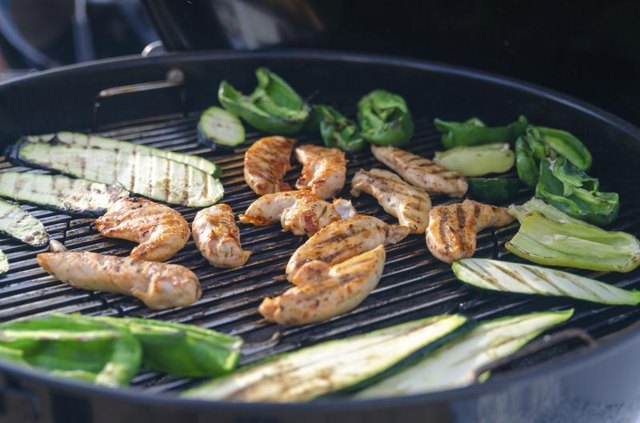 A grill with chicken and vegetables cooking. A grill with chicken and vegetables cooking.
