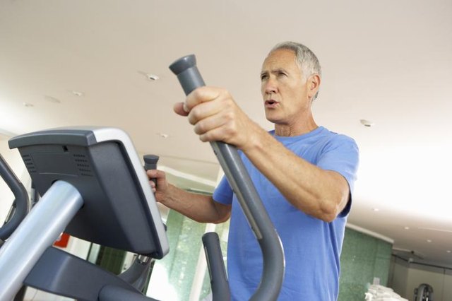A mature man is using the elliptical machine at the gym. A mature man is using the elliptical machine at the gym.