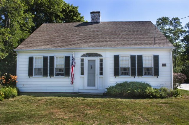 A white cape home with an American flag displayed. A white cape home with an American flag displayed.