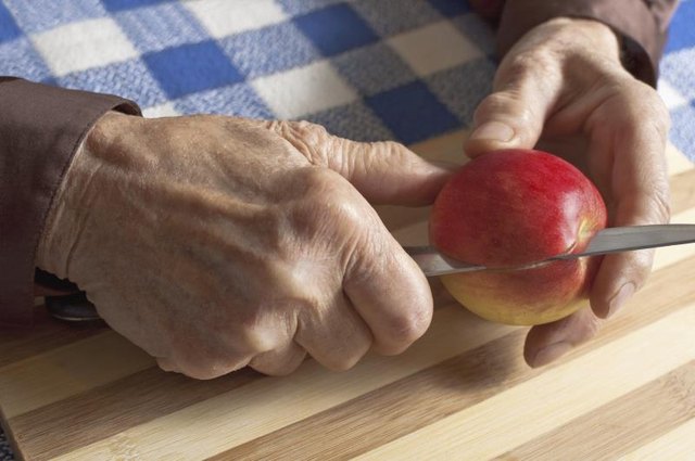 A close-up of a woman with arthritic hands slicing an apple. A close-up of a woman with arthritic hands slicing an apple.